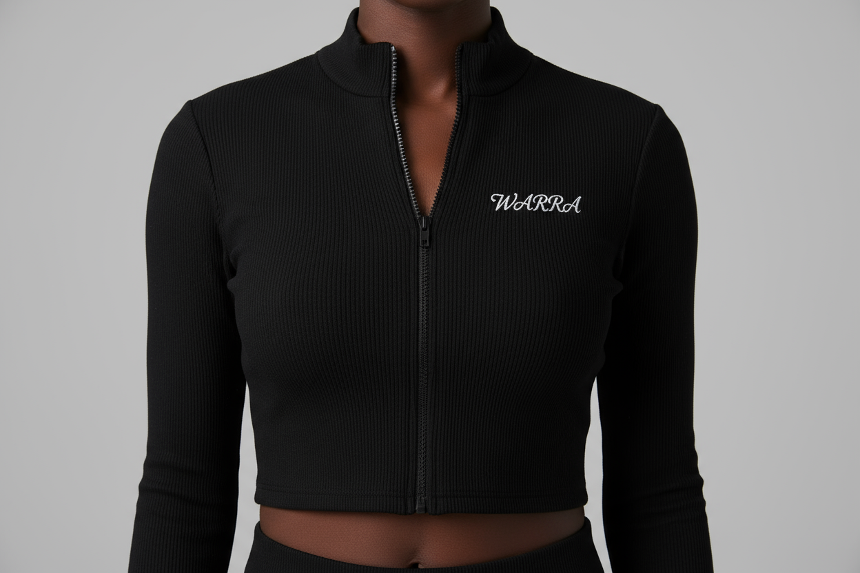 CLOSE-UP STUDIO PHOTO OF A BLACK & wHITE FEMALE MODEL WEARING A BLACK RIBBED LONG-SLEEVE CROPPED ZIP TOP LIKE THE REFERENCE IMAGE.
FABRIC TEXTURE MUST BE CLEAR — TIGHT RIBBED KNIT, SMOOTH AND STRETCHY.
“WARRA” WRITTEN IN SMALL WHITE CURSIVE ACROSS THE UPPER CHEST, CENTERED LIKE A NIKE LOGO.
THE CURSIVE FONT MUST BE REALISTIC, FLOWING, AND ELEGANT WITH A DISTINCT “W”.
SOFT STUDIO LIGHTING, NEUTRAL BACKGROUND, FOCUS ON FABRIC AND LOGO DETAIL.
NO TEXT, NO DISTRACTIONS, JUST MODEL AND TOP.
